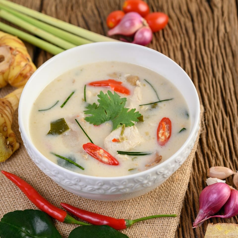 Creamy Thai coconut soup (Tom Kha Gai) with chicken, red chilies, and cilantro in a white bowl.