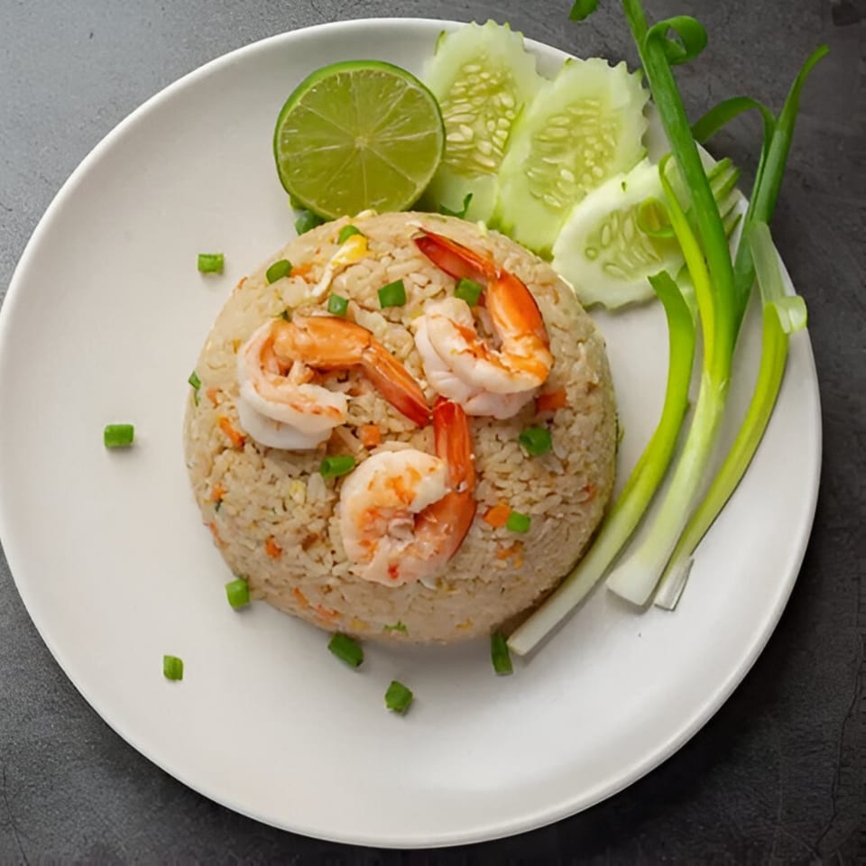 Thai shrimp fried rice with lime, cucumber, and green onions on a white plate.