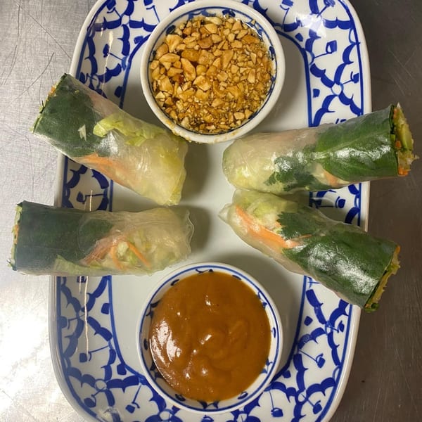 Four fresh spring rolls with peanut sauce and crushed peanuts on a white and blue patterned plate.