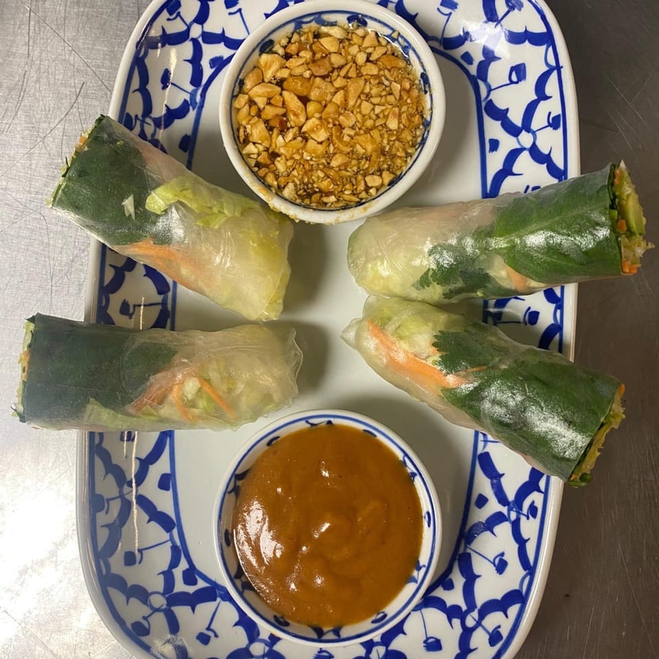 Four fresh spring rolls with peanut sauce and crushed peanuts on a white and blue patterned plate.