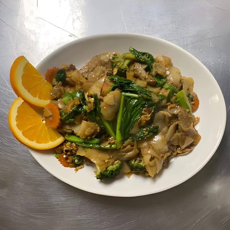 Lina Street Food's Thai dish with noodles, meat, green vegetables, and orange slices on a white plate.