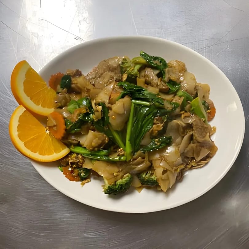 Lina Street Food's Thai dish with noodles, meat, green vegetables, and orange slices on a white plate.