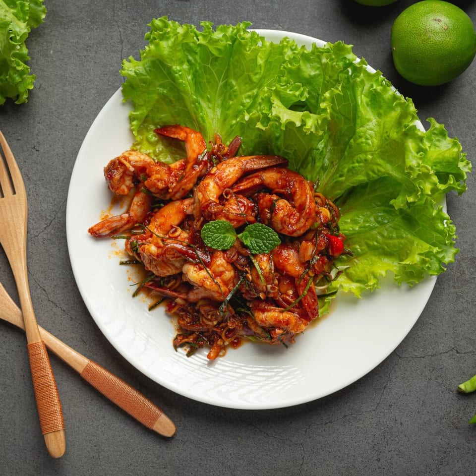 Spicy Thai shrimp stir-fry with herbs and lettuce on a white plate, with limes nearby.