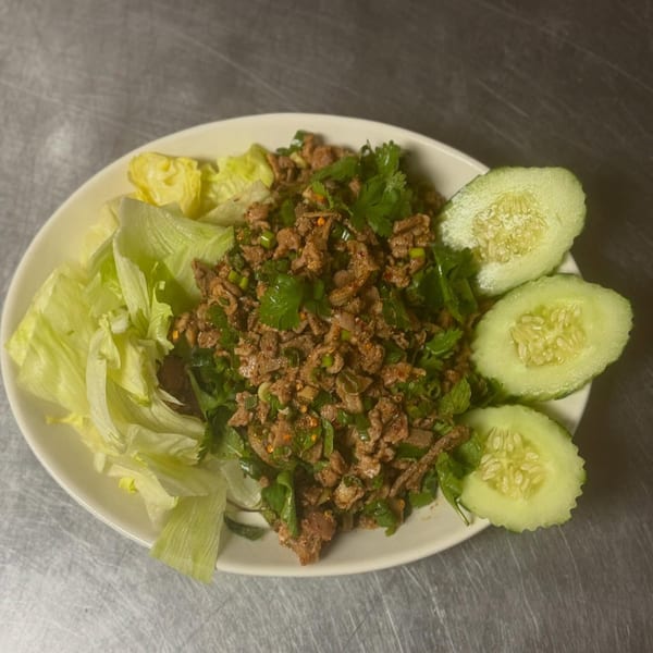 Larb, a Thai minced meat salad with herbs, lettuce, and cucumber slices on a white plate.