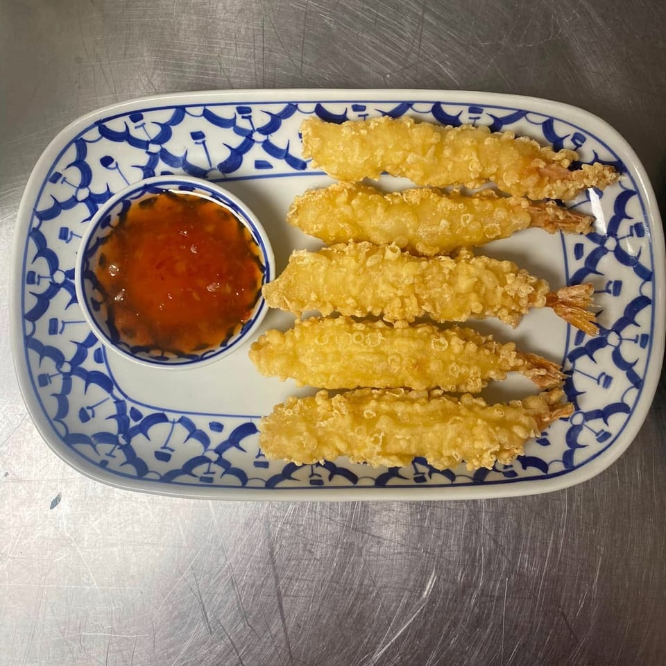 Five crispy fried shrimp with sweet chili dipping sauce on a blue and white patterned plate.