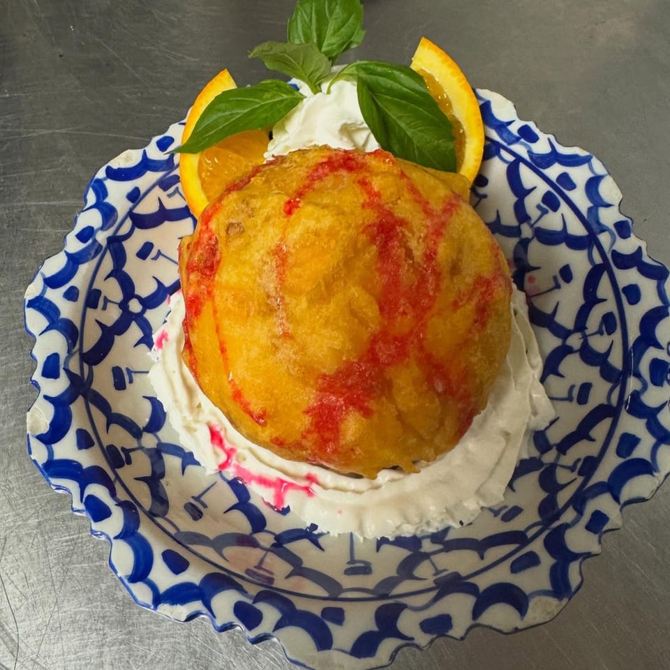 Fried ice cream dessert with red syrup, whipped cream, orange slices, and basil on a blue and white plate.